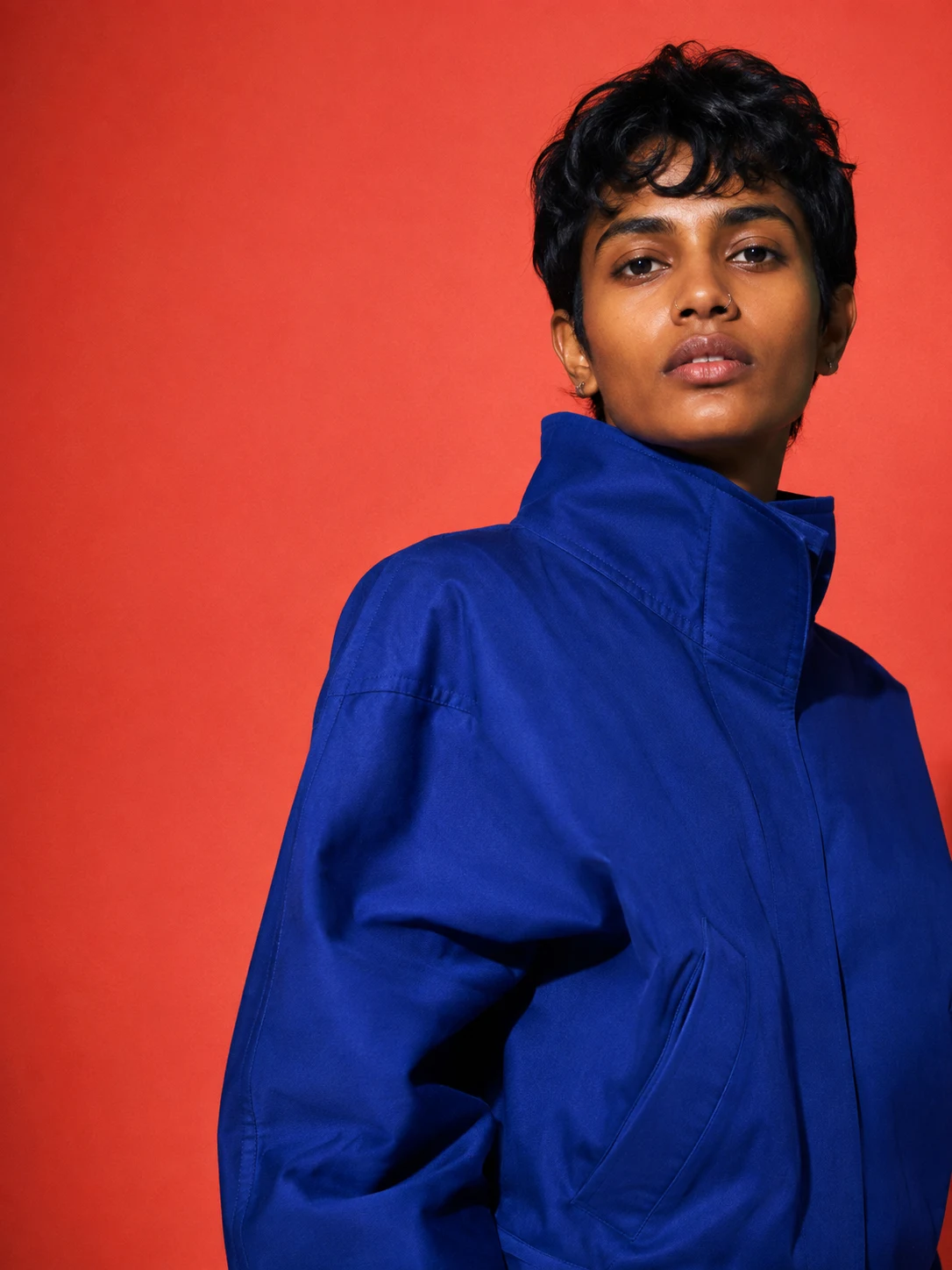 An adult in a cobalt jacket, photographed against a coral studio backdrop