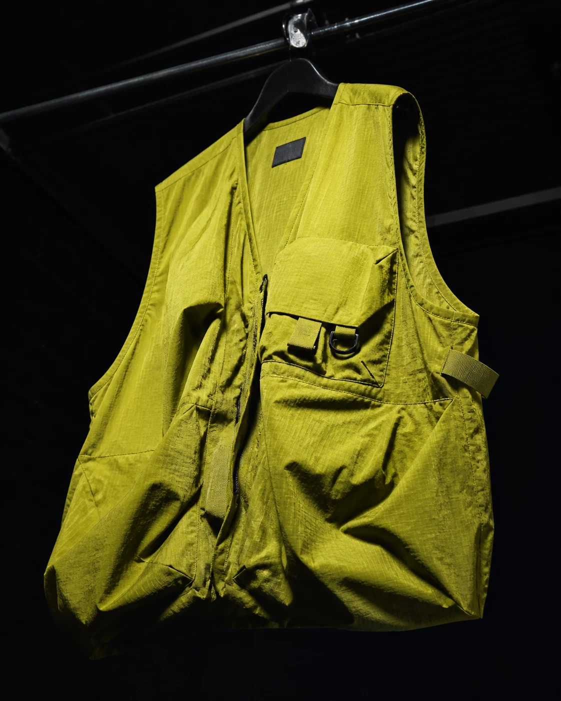 An acid-chartreuse technical utility vest with visible seams and hardware in a dark studio.